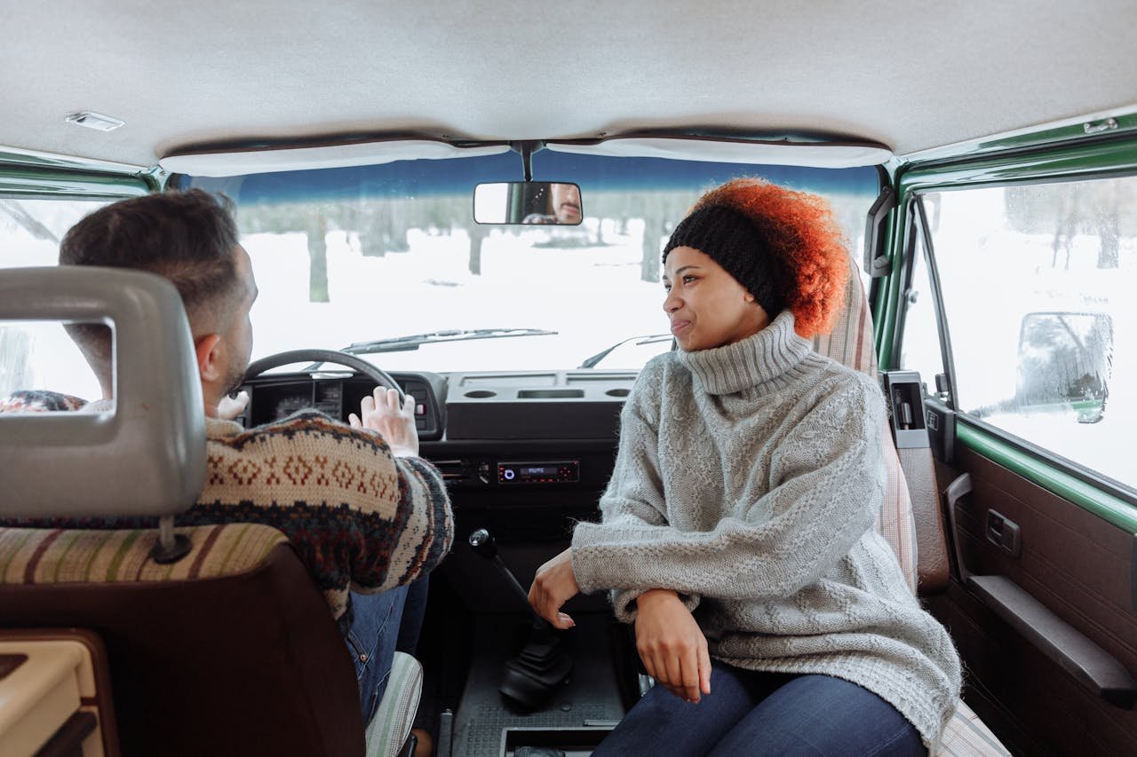 Two people enjoying a winter road trip inside a camper van, showcasing warmth and adventure.